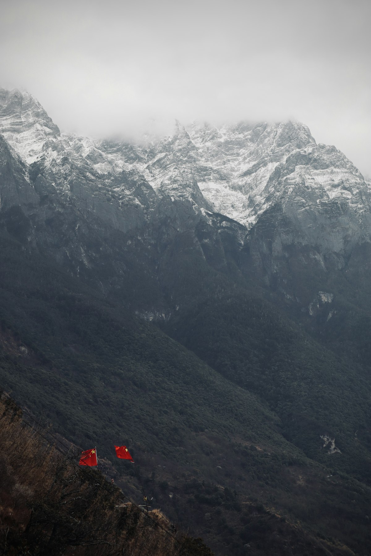 The High Trail at Tiger Leaping Gorge — a narrow path suspended between Jade Dragon Snow Mountain and Haba Snow Mountain, with prayer flags against snow-capped peaks